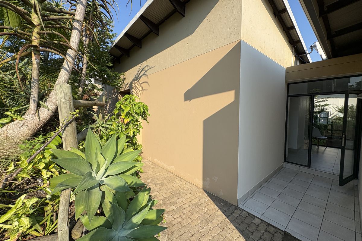A view of the exterior side walkway featuring paved flooring, a covered entrance area, and established garden landscaping.