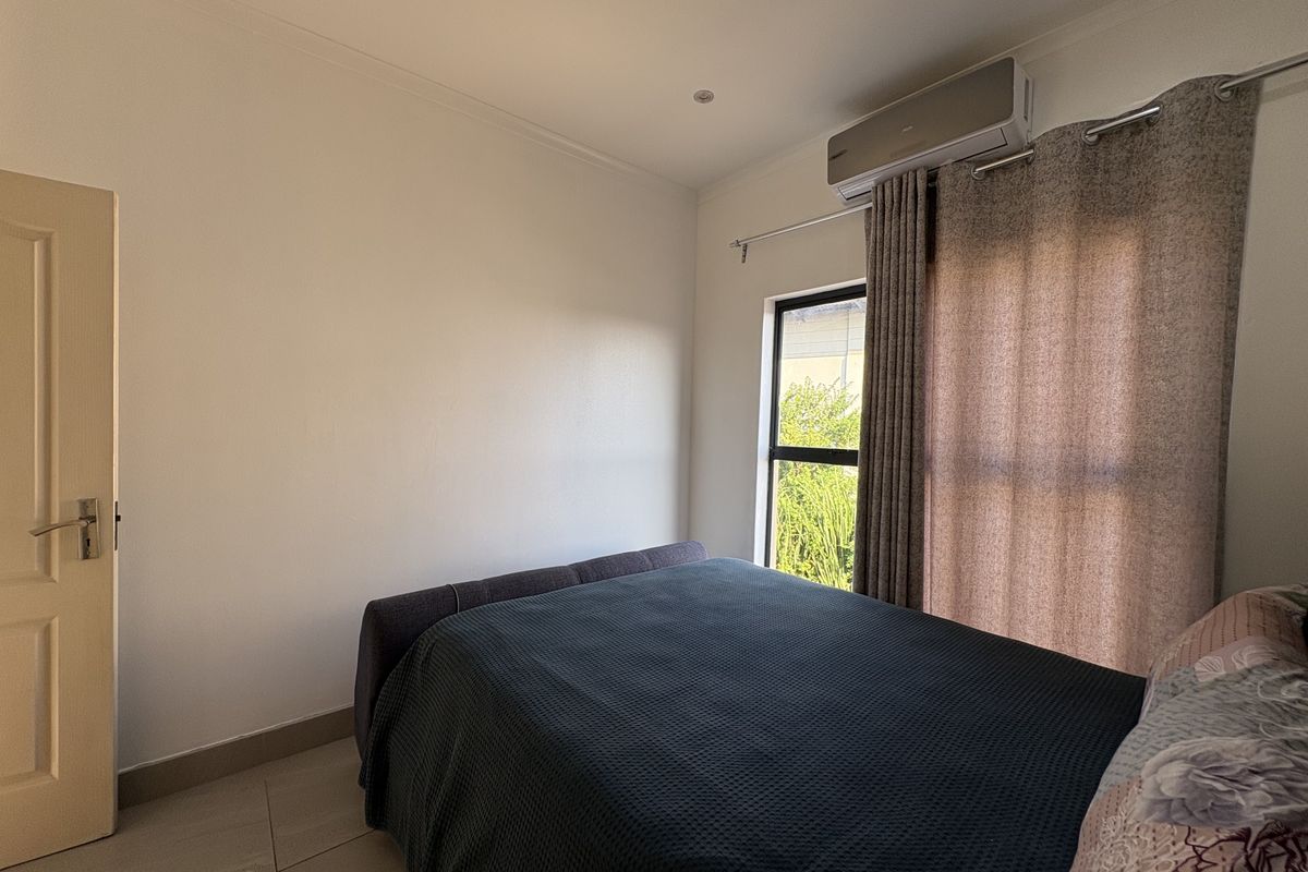A well-maintained bedroom featuring tiled flooring, a wall-mounted air conditioning unit, and a window with curtain fixtures.