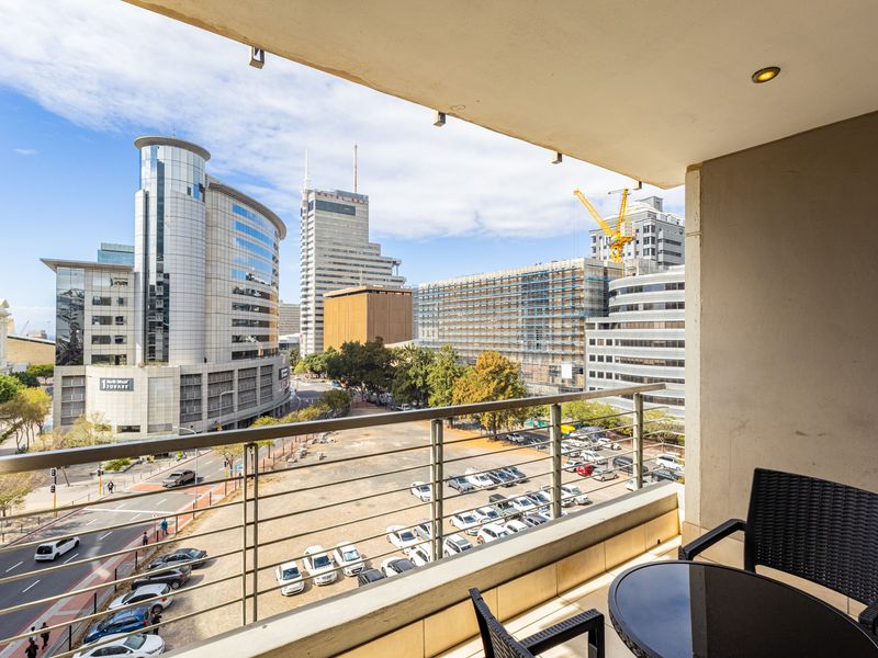 A covered balcony featuring a metal balustrade and recessed lighting, offering an expansive urban view of the surrounding city skyline.