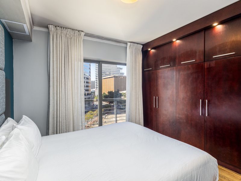 A well-maintained bedroom featuring extensive dark wood built-in cupboards, recessed lighting, and a sliding door leading to a balcony with city views.