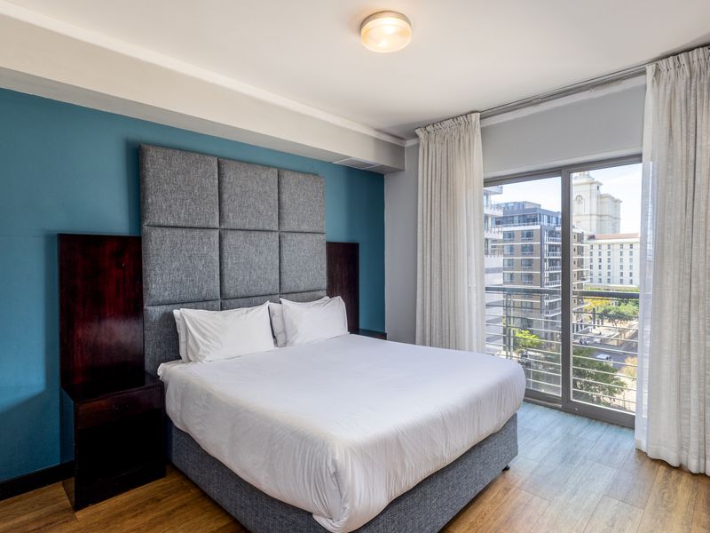 A well-maintained bedroom featuring laminate flooring, a feature wall, and a sliding glass door providing access to a balcony with city views.