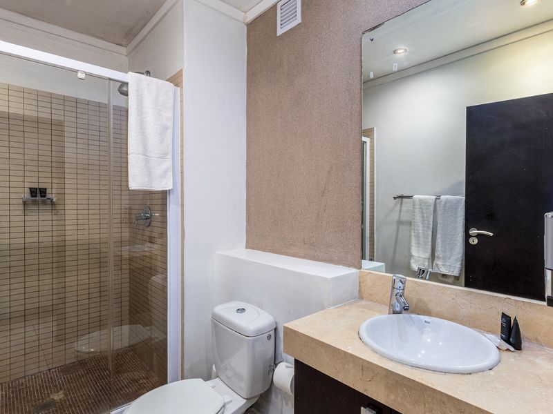 A functional bathroom featuring a glass-enclosed shower, stone-topped vanity with basin, and wall-mounted mirror, presenting a clean and well-maintained space.