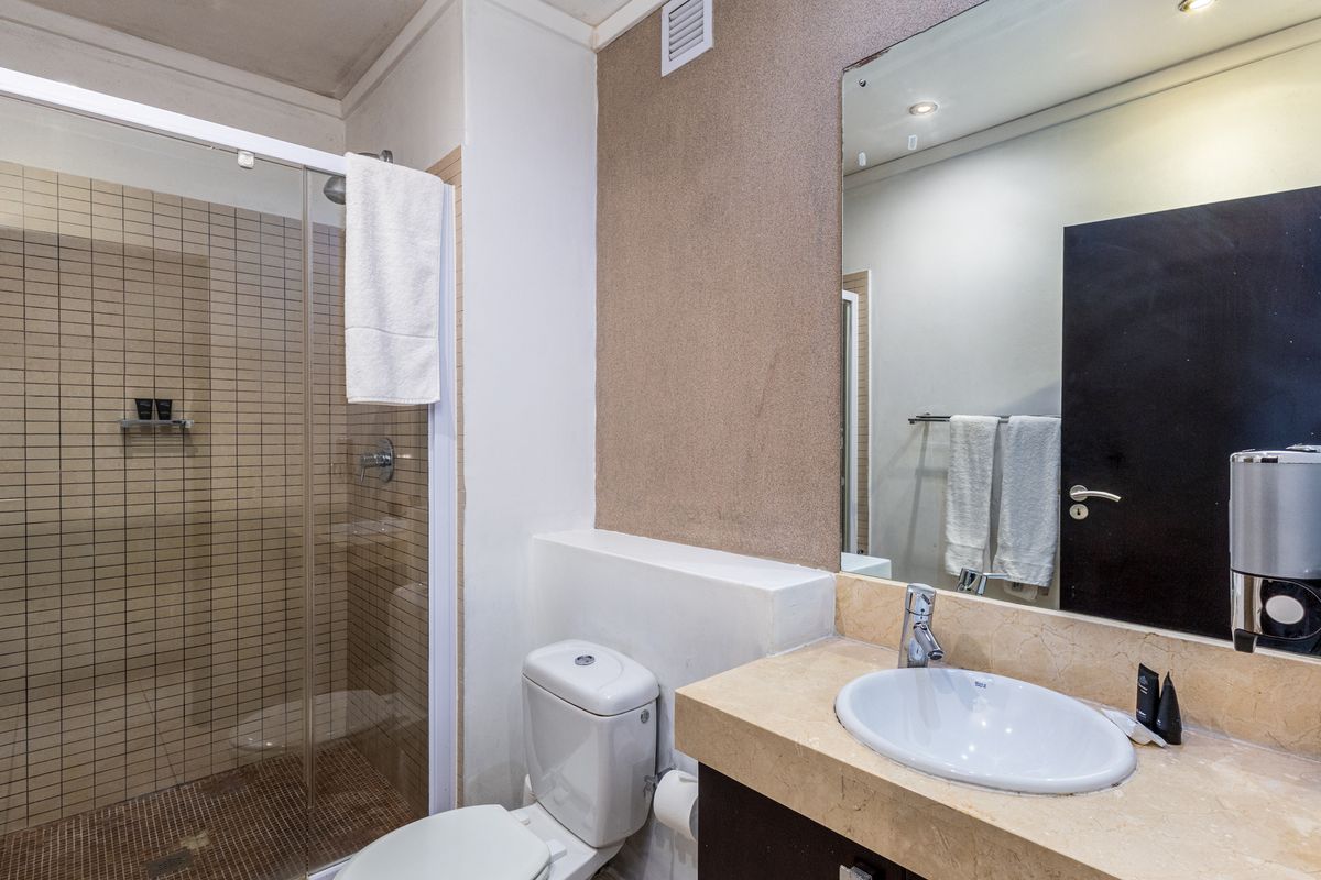 A functional bathroom featuring a glass-enclosed shower, stone-topped vanity with basin, and wall-mounted mirror, presenting a clean and well-maintained space.