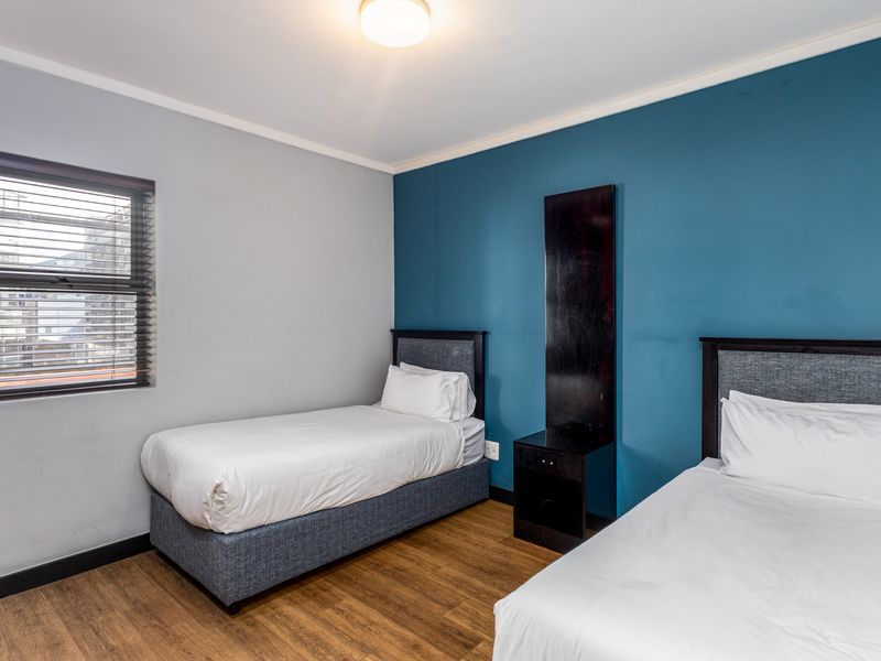 A bedroom featuring laminate flooring, a blue accent wall, and a window with venetian blinds.