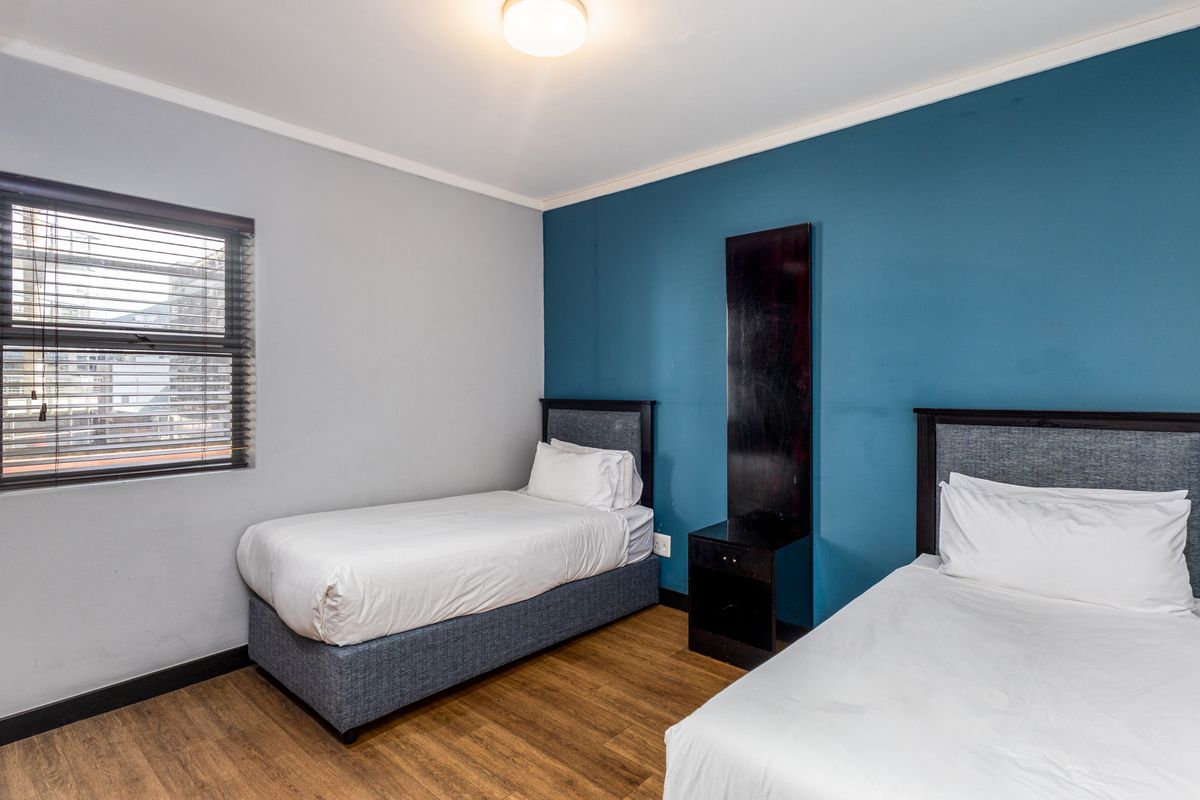 A bedroom featuring laminate flooring, a blue accent wall, and a window with venetian blinds.