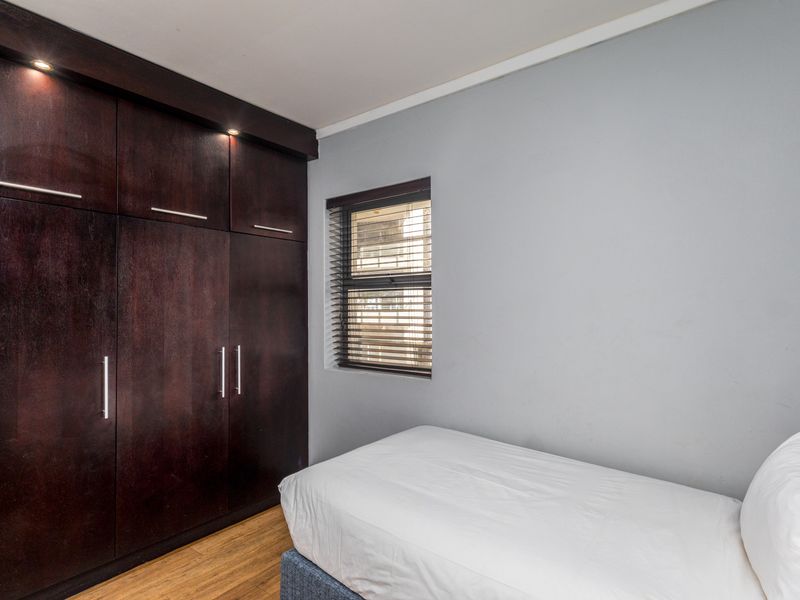 A well-maintained bedroom featuring dark wood built-in cabinetry with integrated lighting, laminate flooring, and a window fitted with venetian blinds.