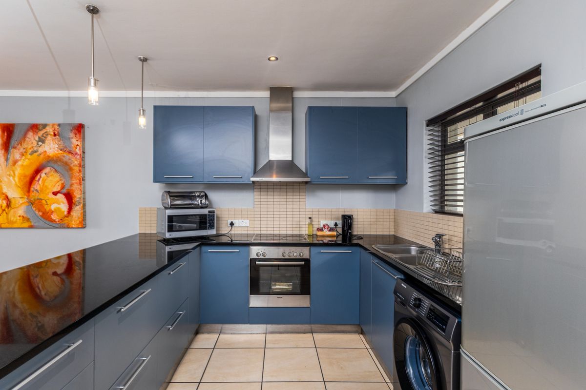 Modern kitchen featuring blue cabinetry, granite countertops, stainless steel appliances, tiled backsplash, and integrated laundry plumbing.