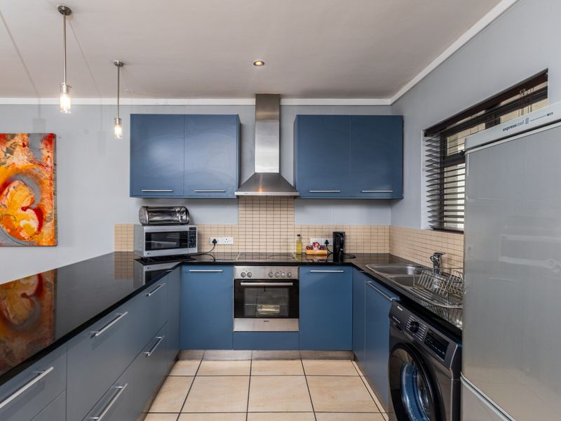 Modern kitchen featuring blue cabinetry, granite countertops, stainless steel appliances, tiled backsplash, and integrated laundry plumbing.
