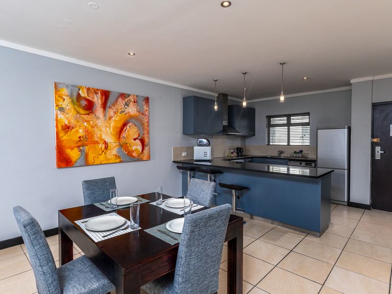 Open-plan kitchen and dining area featuring dark blue cabinetry, granite countertops, breakfast bar, and tiled flooring throughout.
