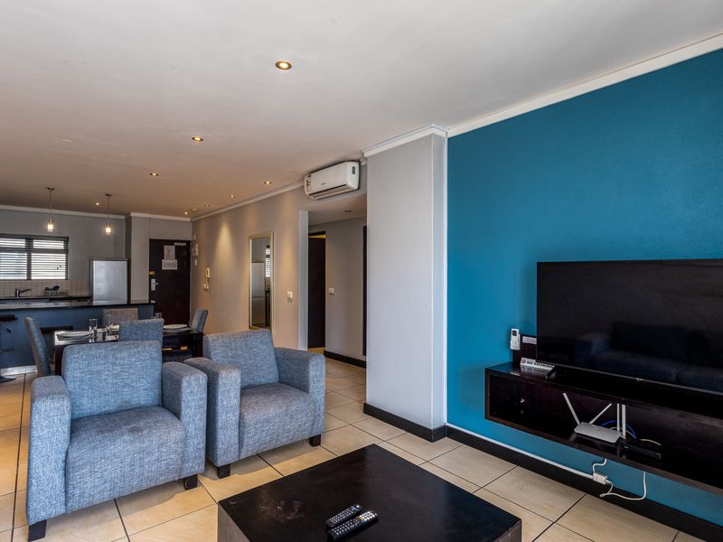 An open-plan living and kitchen area featuring tiled floors, recessed lighting, a wall-mounted air conditioner, and a modern blue accent wall.
