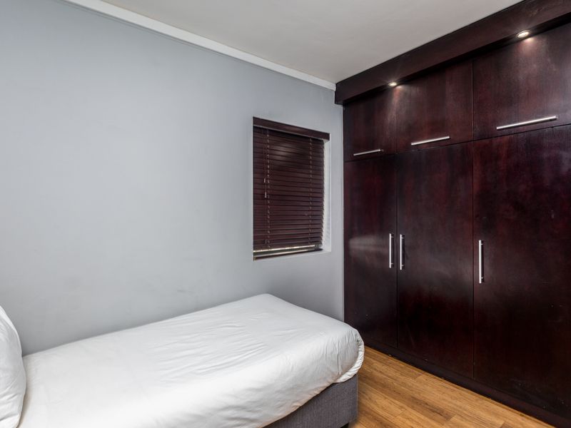 A well-maintained bedroom featuring dark wood built-in cupboards, recessed downlighting, timber flooring, and a window with venetian blinds.