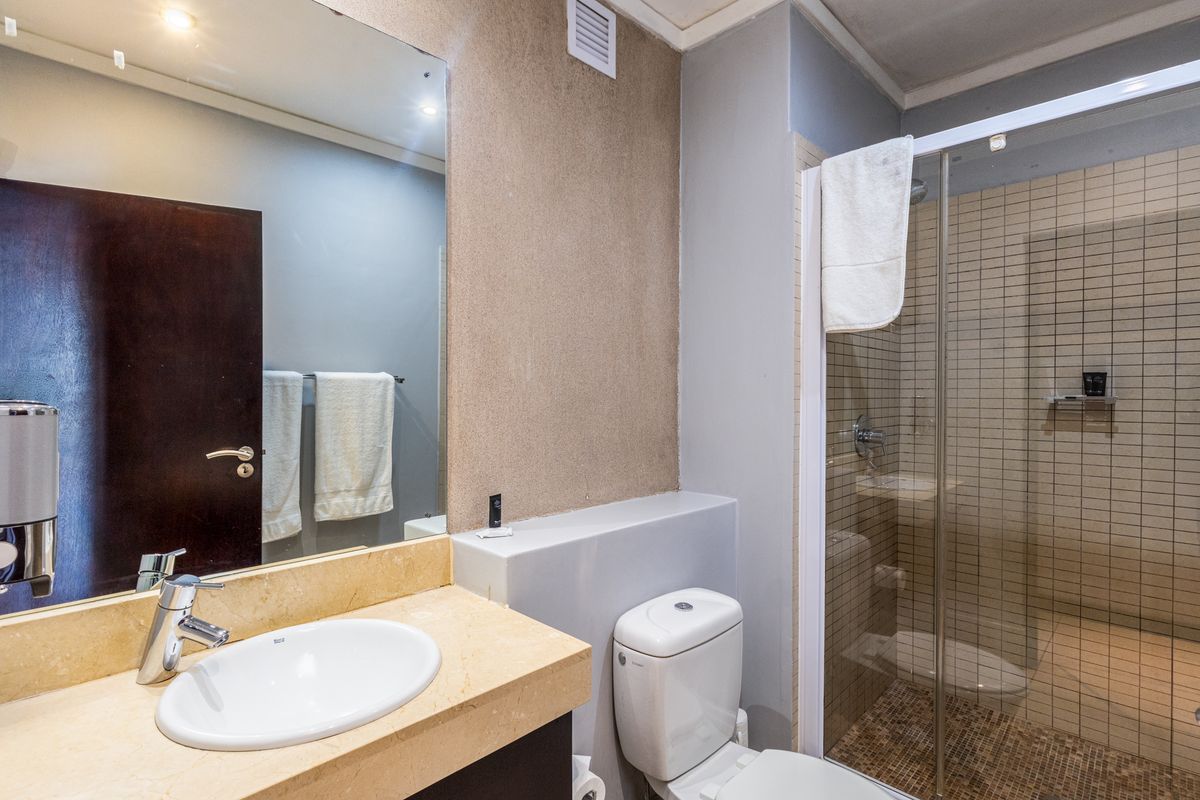 A functional bathroom featuring a stone-topped vanity, a glass-enclosed shower with tiled finishes, and a standard toilet.