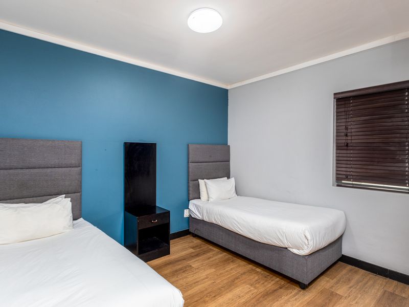 A well-maintained bedroom featuring laminate flooring, a blue accent wall, and venetian blinds, providing a clean and functional living space.