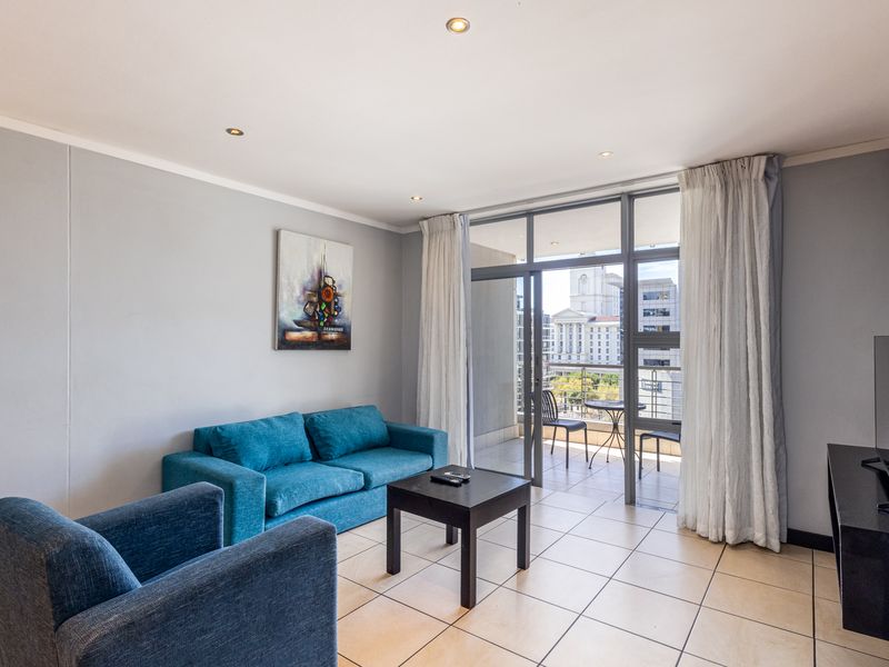 A bright living room featuring tiled flooring, recessed lighting, and a large sliding glass door providing access to a private balcony with city views.