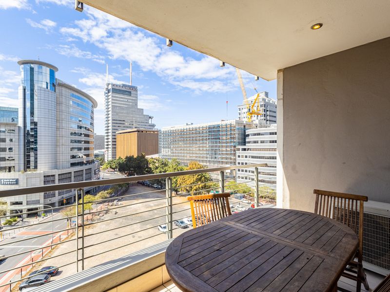 A covered balcony featuring a metal balustrade and an integrated air conditioning unit, offering an expansive urban city view.
