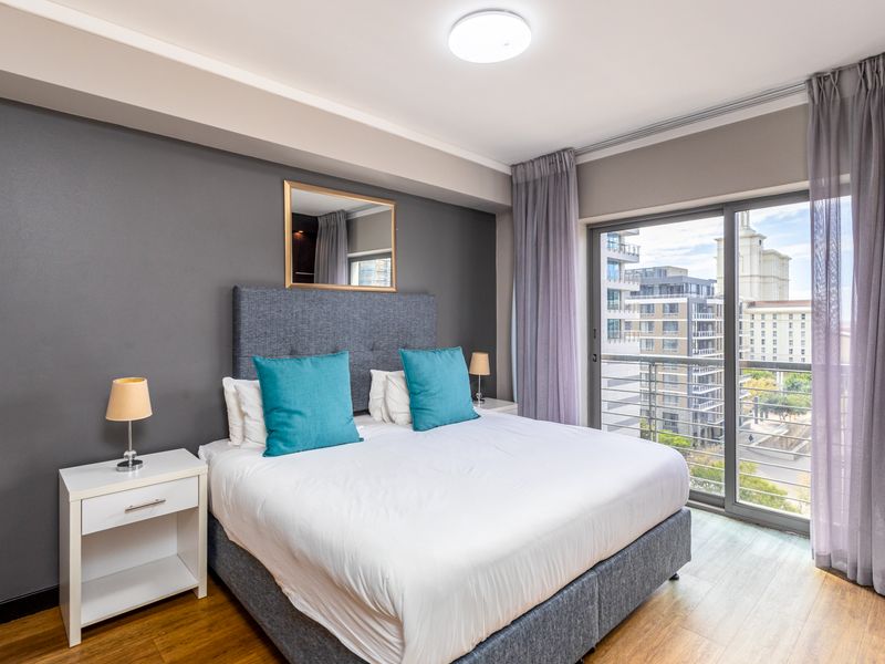A well-maintained bedroom featuring laminate flooring, a feature wall, and a sliding glass door providing access to a private balcony with city views.