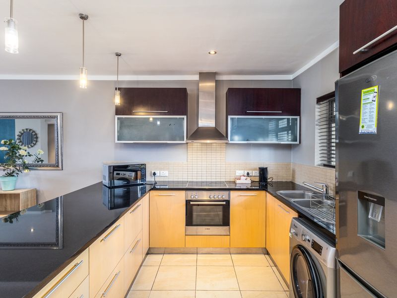 Modern kitchen featuring granite countertops, built-in oven, electric hob, stainless steel extractor fan, and ample cabinetry with tiled flooring and backsplash.