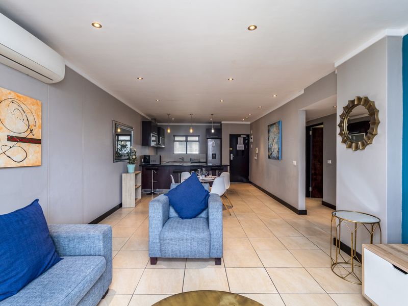 Spacious open-plan living and kitchen area featuring neutral tiled flooring, recessed lighting, and a modern split-system air conditioning unit.