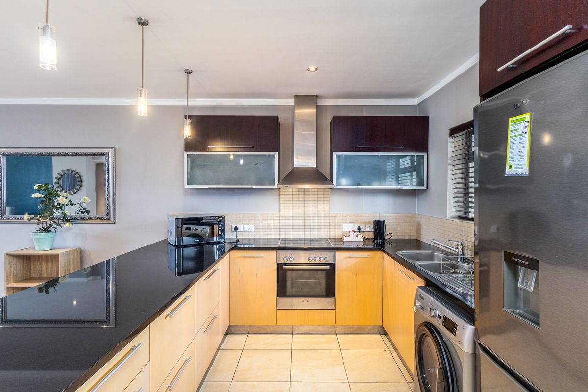 Modern kitchen featuring granite countertops, built-in oven, electric hob, stainless steel extractor fan, and ample cabinetry with tiled flooring and backsplash.
