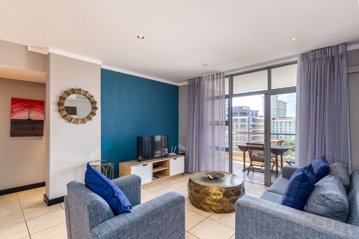 A bright living room featuring tiled floors, a bold blue accent wall, and large sliding glass doors leading to a private balcony.
