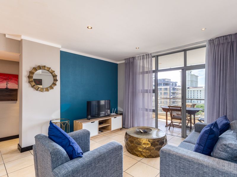A bright living room featuring tiled floors, a bold blue accent wall, and large sliding glass doors leading to a private balcony.