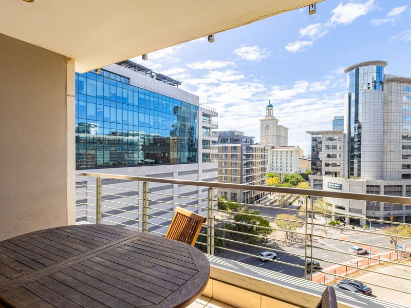 A covered balcony featuring a stainless steel balustrade and tiled flooring, offering an elevated urban view of the surrounding city buildings.
