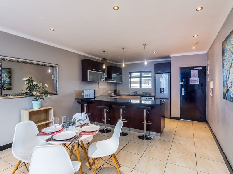 Modern open-plan kitchen and dining area featuring dark wood cabinetry, granite countertops, a breakfast bar, and tiled flooring throughout.