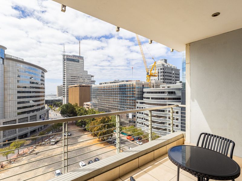 A covered balcony featuring tiled flooring and a metal balustrade, offering an elevated urban view of the surrounding city skyline.