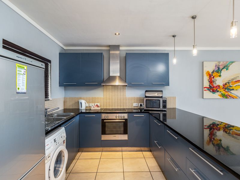 Modern kitchen featuring blue cabinetry, granite countertops, stainless steel appliances, tiled backsplash, and a breakfast bar with pendant lighting.
