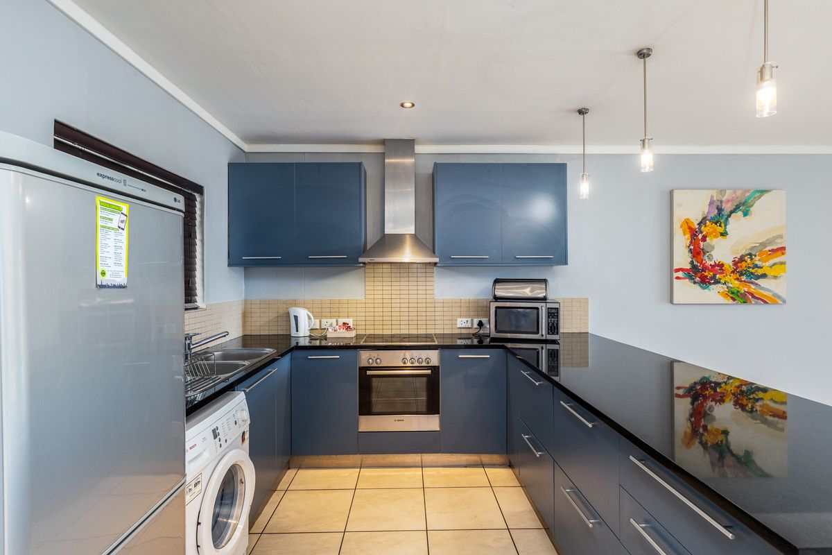 Modern kitchen featuring blue cabinetry, granite countertops, stainless steel appliances, tiled backsplash, and a breakfast bar with pendant lighting.