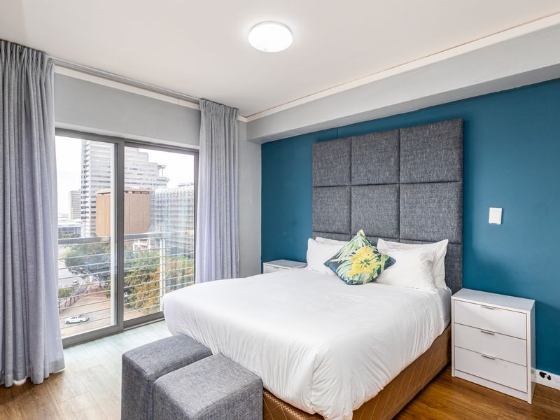 A well-maintained bedroom featuring laminate flooring, a bold blue accent wall, and a sliding glass door providing access to a private balcony.