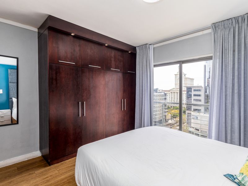 A well-maintained bedroom featuring dark wood built-in wardrobes, laminate flooring, and a sliding glass door providing access to a balcony with city views.