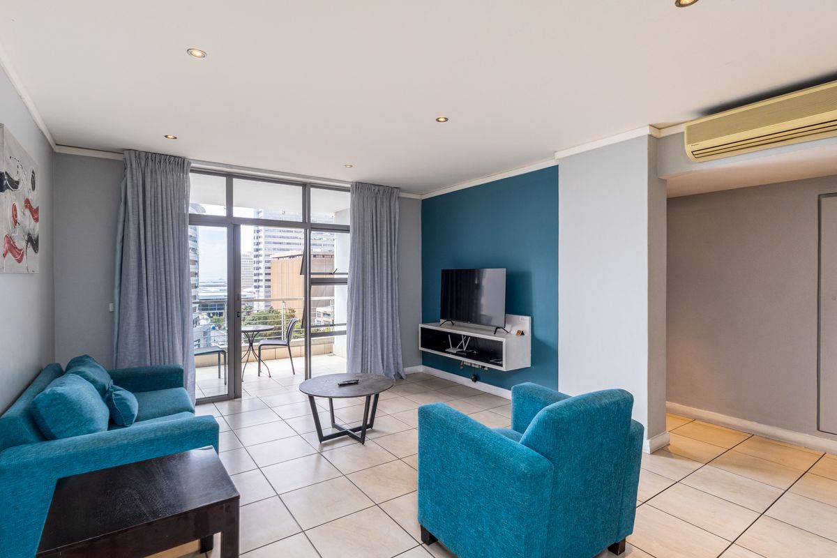 A bright living room featuring tiled floors, a blue accent wall, and direct access to a balcony with city views.
