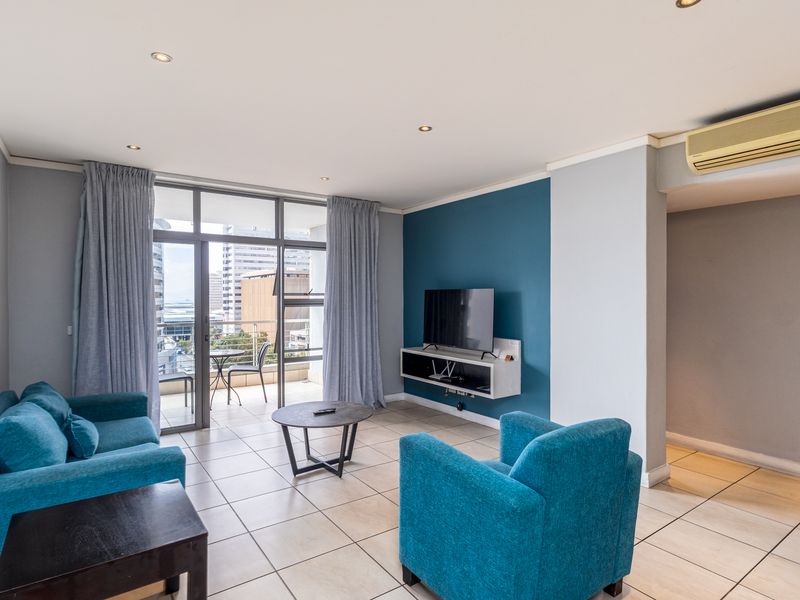 A bright living room featuring tiled floors, a blue accent wall, and direct access to a balcony with city views.