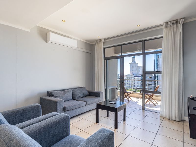 Bright living room featuring tiled flooring, a wall-mounted air conditioning unit, and large sliding glass doors opening onto a private balcony with city views.