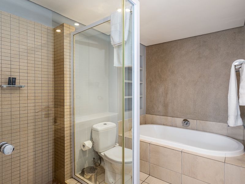 A modern bathroom featuring a glass-enclosed shower, a built-in bathtub with tiled surround, and a separate toilet area with neutral finishes.