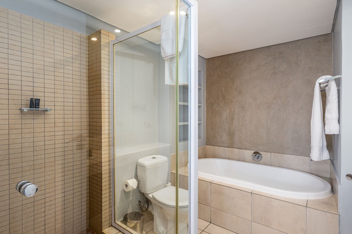 A modern bathroom featuring a glass-enclosed shower, a built-in bathtub with tiled surround, and a separate toilet area with neutral finishes.