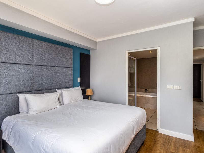 A well-maintained bedroom featuring a large upholstered headboard, laminate flooring, and direct access to an en-suite bathroom.