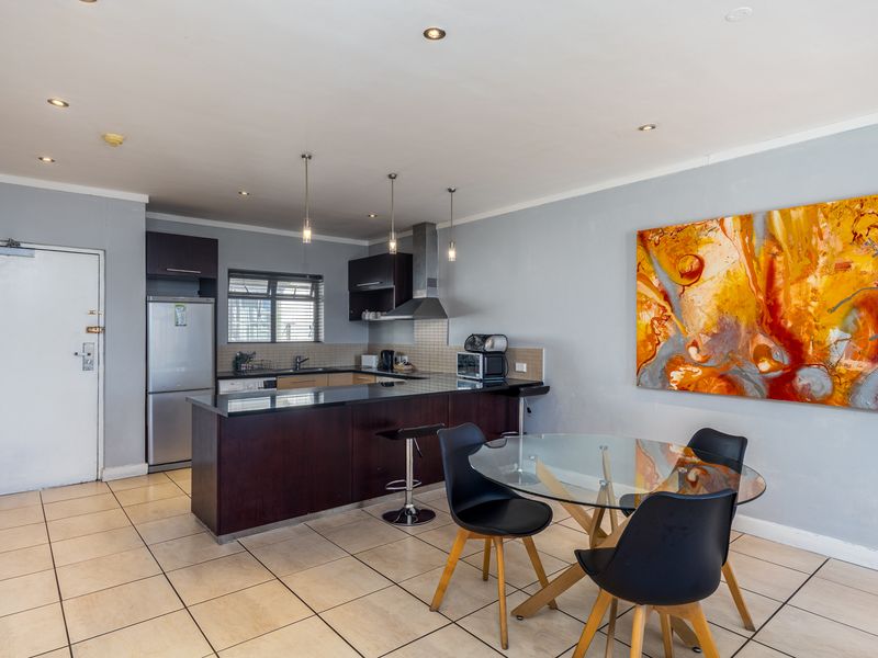 Open-plan kitchen and dining area featuring dark wood cabinetry, granite countertops, a breakfast bar, and tiled flooring throughout.