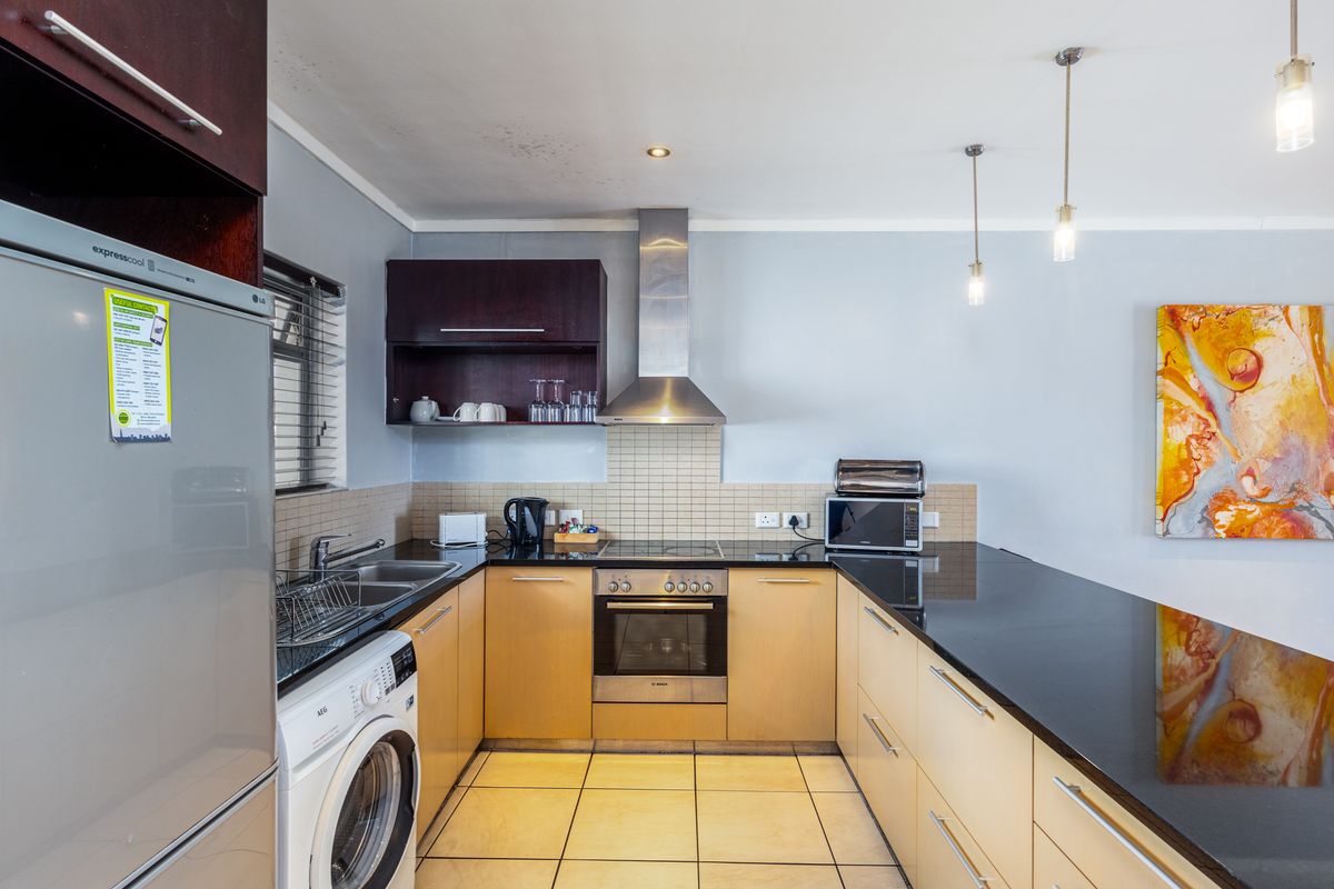 A functional kitchen featuring light wood cabinetry, black granite countertops, integrated stainless steel appliances, and a tiled backsplash with modern pendant lighting.