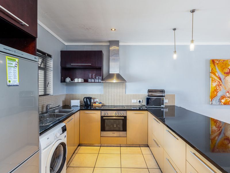 A functional kitchen featuring light wood cabinetry, black granite countertops, integrated stainless steel appliances, and a tiled backsplash with modern pendant lighting.