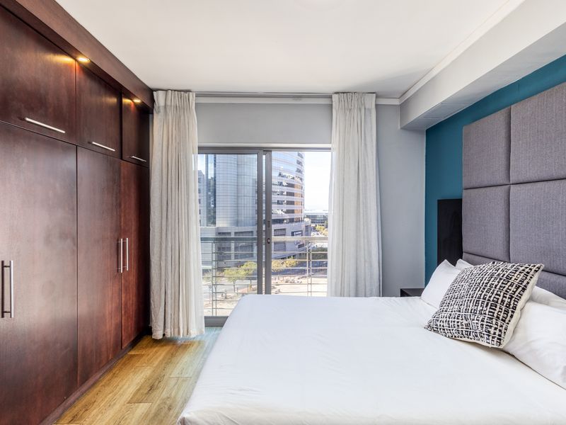 Modern bedroom featuring extensive built-in dark wood cabinetry, laminate flooring, and a sliding glass door leading to a balcony with city views.
