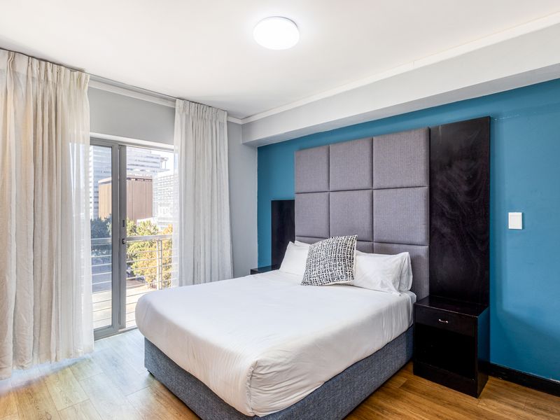 A well-maintained bedroom featuring laminate flooring, a modern built-in headboard, and direct access to a private balcony with city views.