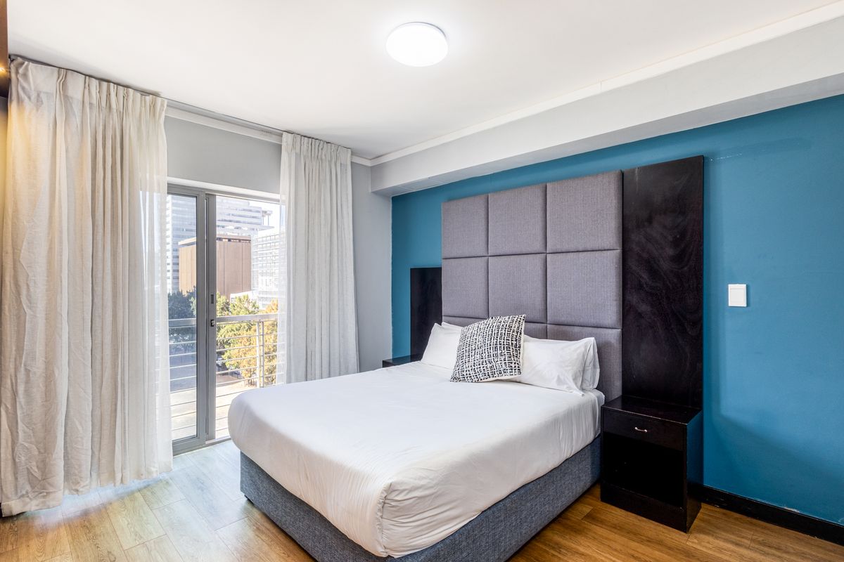 A well-maintained bedroom featuring laminate flooring, a modern built-in headboard, and direct access to a private balcony with city views.