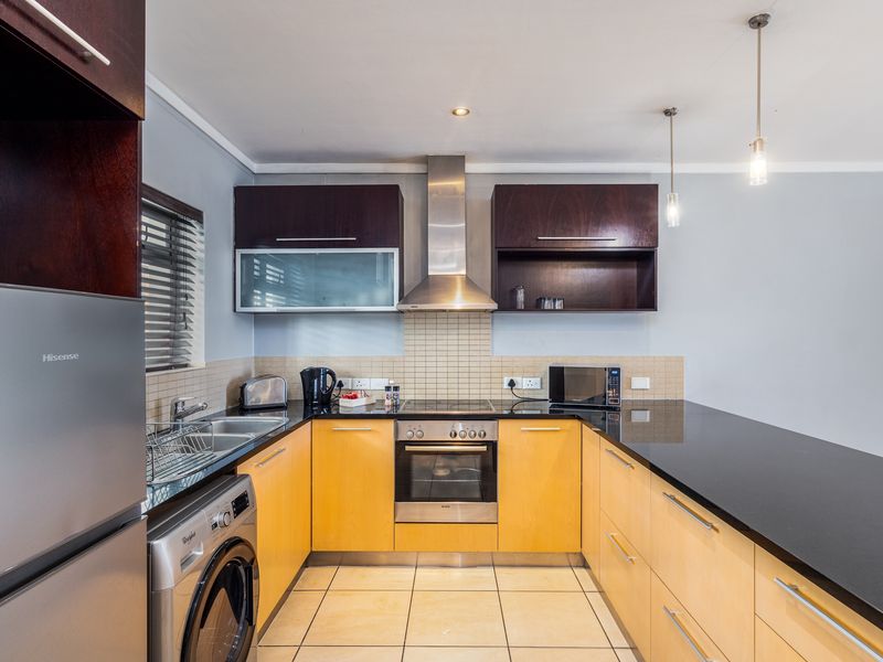 Modern kitchen featuring light wood cabinetry, dark granite countertops, stainless steel appliances, tiled backsplash, and functional layout with integrated sink and hob.