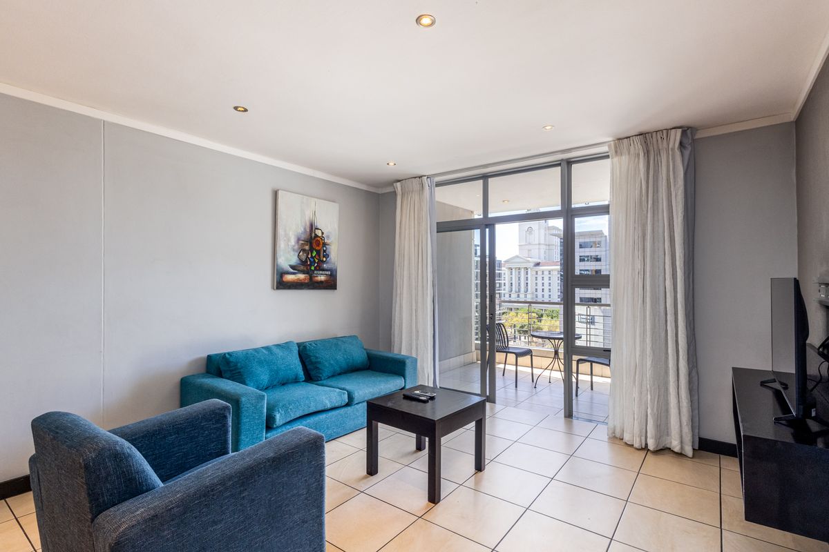 A bright living room featuring tiled flooring, recessed lighting, and a large sliding glass door providing access to a private balcony with city views.