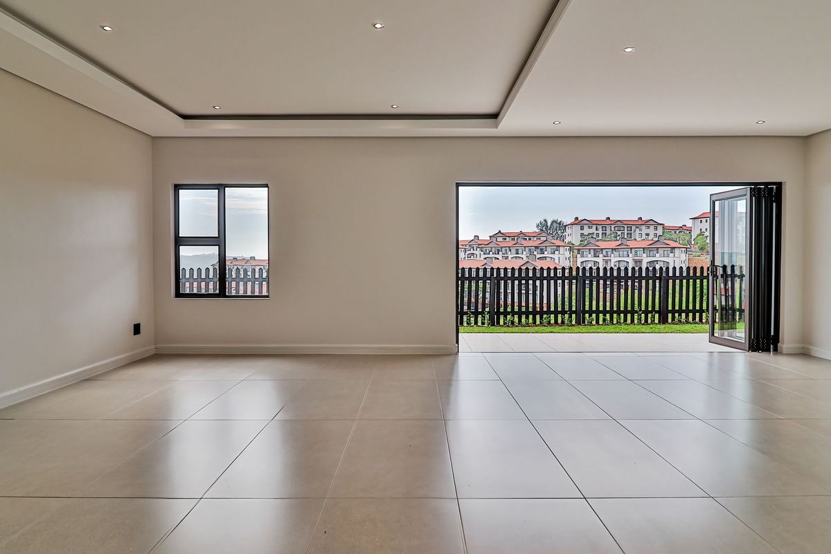 Spacious, light-filled living area featuring large format floor tiles, recessed ceiling lighting, and bi-fold doors opening to a private patio with scenic views.