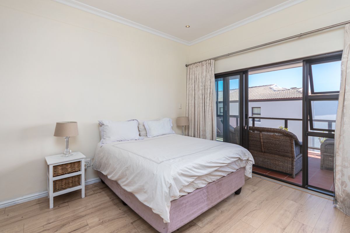A bright bedroom featuring light wood-look flooring, crown molding, and sliding glass doors that open onto a private balcony.