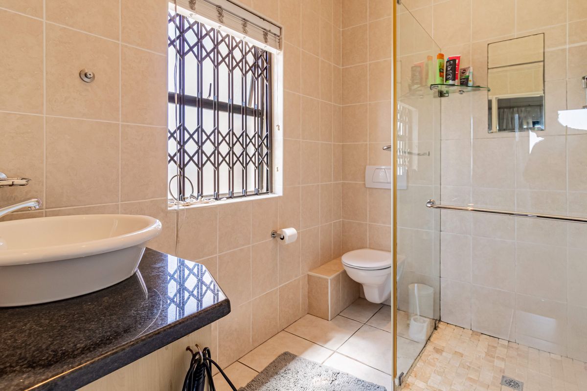 A functional bathroom featuring a vessel sink on a granite vanity, a wall-mounted toilet, and a glass-enclosed shower with tiled walls.