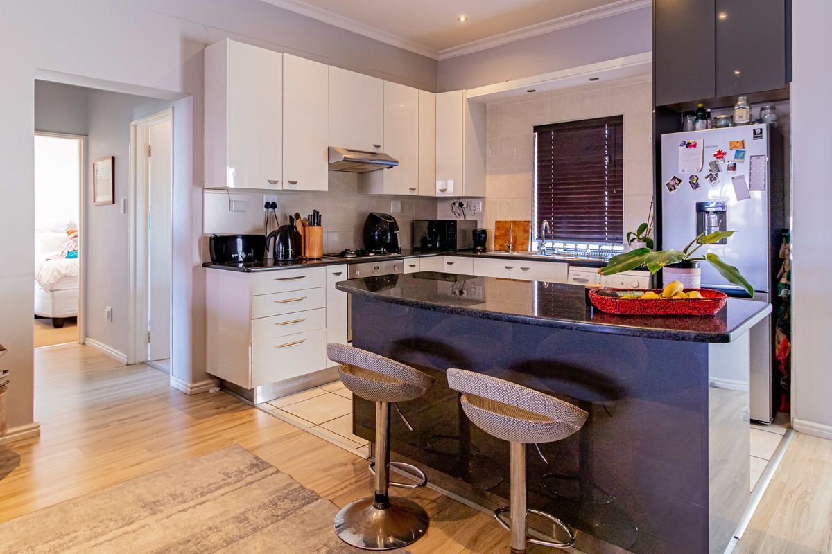 Modern kitchen featuring high-gloss white cabinetry, dark granite countertops, a central breakfast island, and integrated stainless steel appliances.